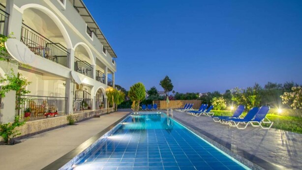 A swimming pool with lounge chairs, a building with balconies, and a clear sky. - Brinswick Private Villa complex (Laganas, Zakynthos)
