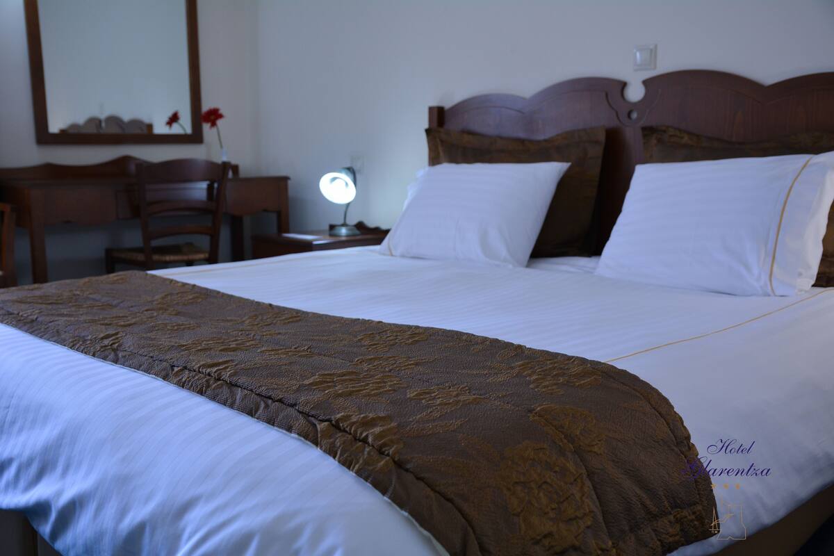 A neatly made bed with a brown headboard and white linens.