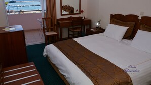 Habitación de hotel con una cama grande, un escritorio, una silla, un aparador y vista al mar.