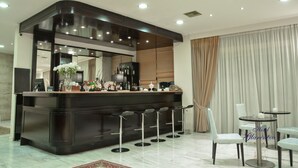 Un área de bar moderna con mostrador oscuro, taburetes y una zona de estar con dos mesas redondas y sillas.