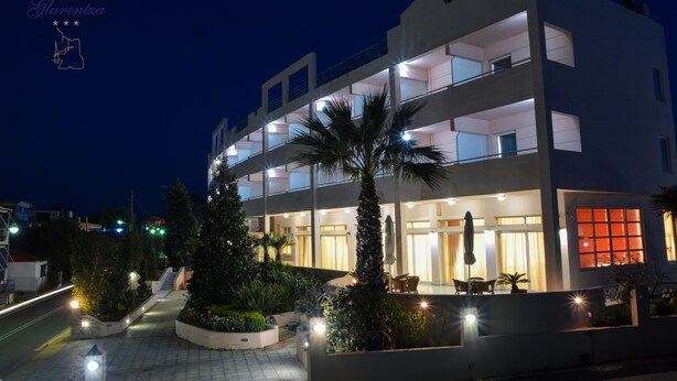 Un hotel de varios pisos con diseño moderno, que cuenta con balcones, una entrada bien iluminada y un patio ajardinado con palmeras y plantas.