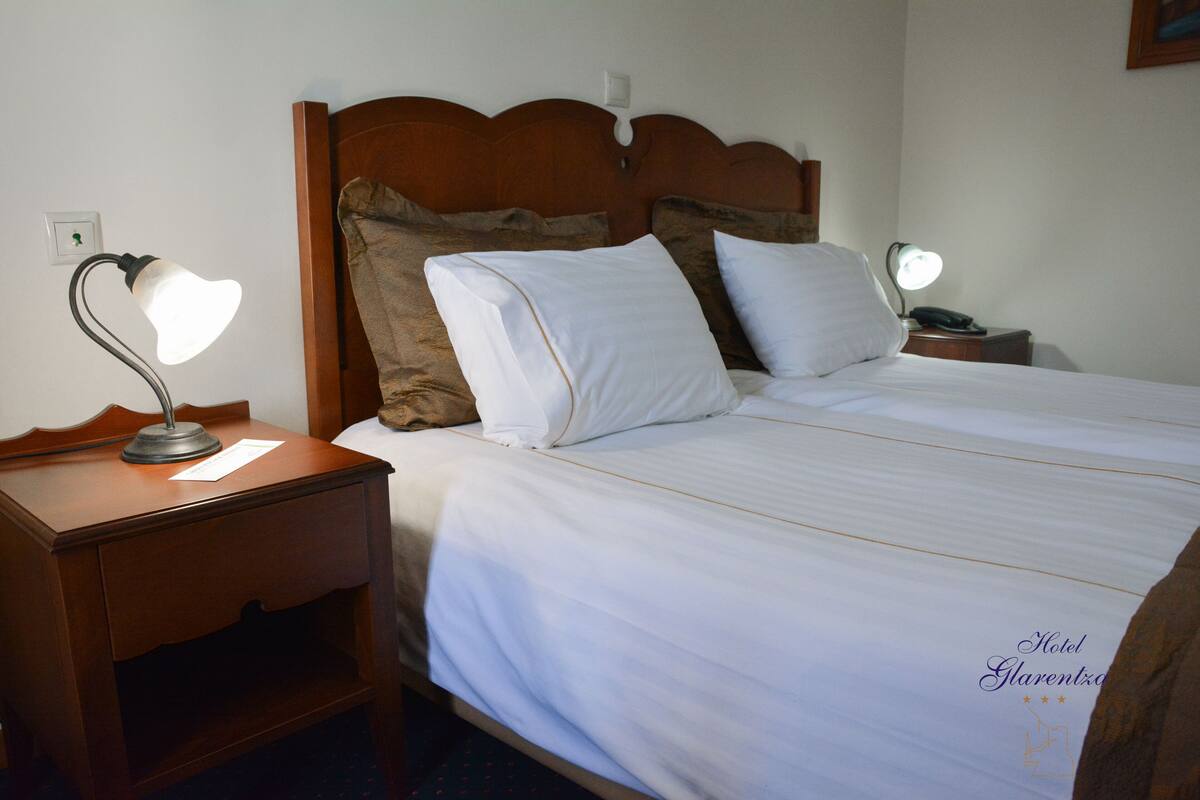 A neatly made bed with white linens, a wooden headboard, and two bedside lamps.
