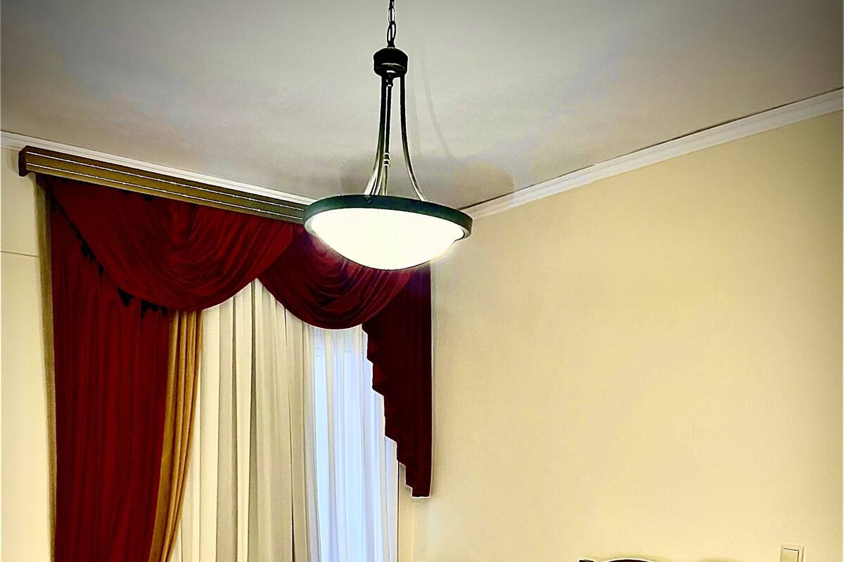 A hotel room with a large bed, red curtains, a desk with a chair, and a hanging light fixture.