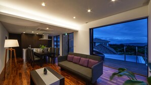 A modern living room with a sofa, dining table, and a large window overlooking a deck.