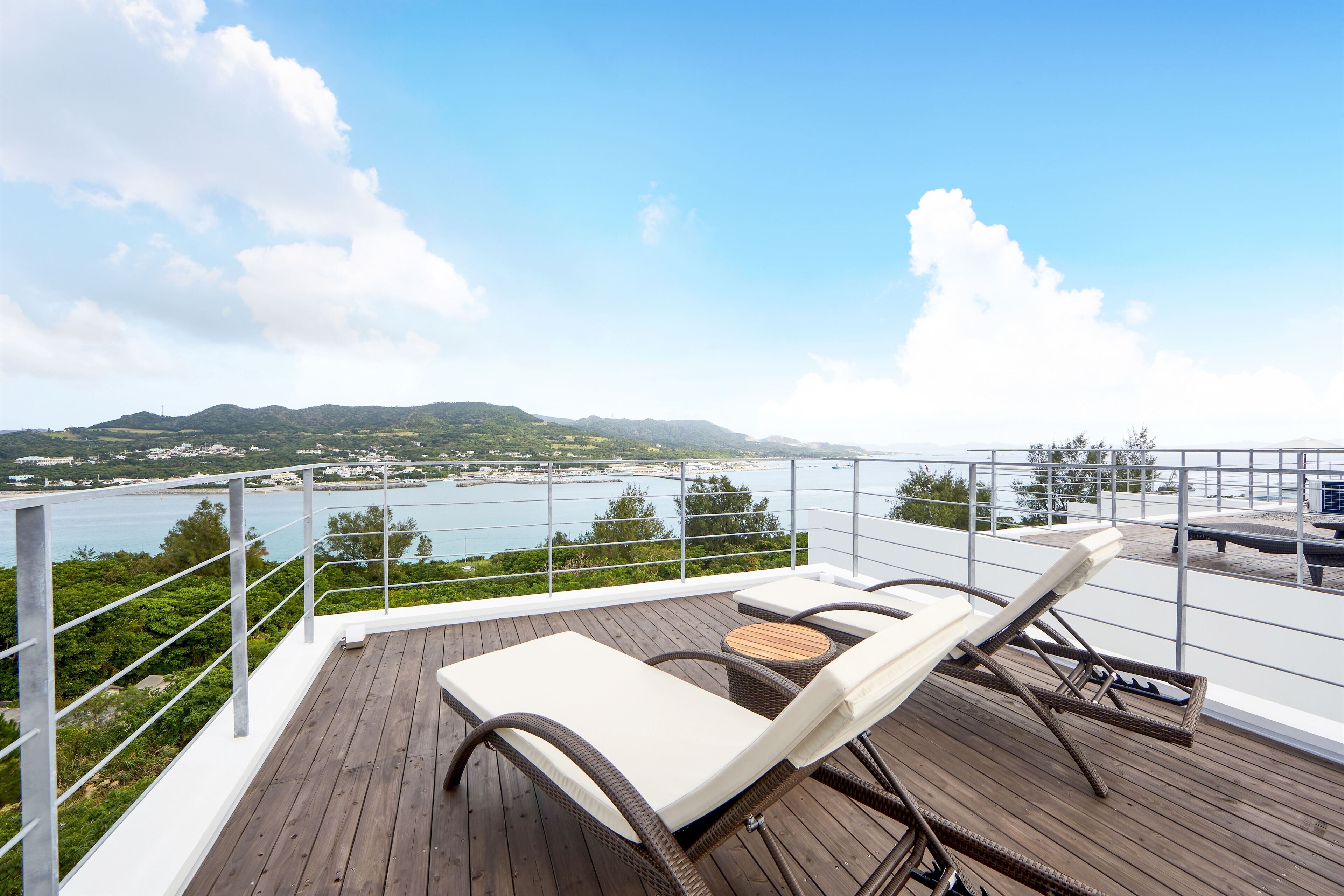 A wooden deck with two lounge chairs and a table overlooking a body of water and distant hills.