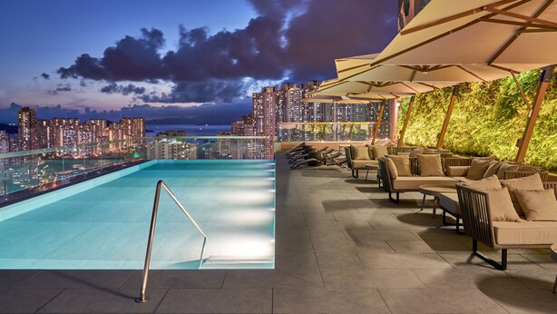 Piscina en la azotea con vistas a la ciudad, mobiliario exterior y un muro ajardinado.