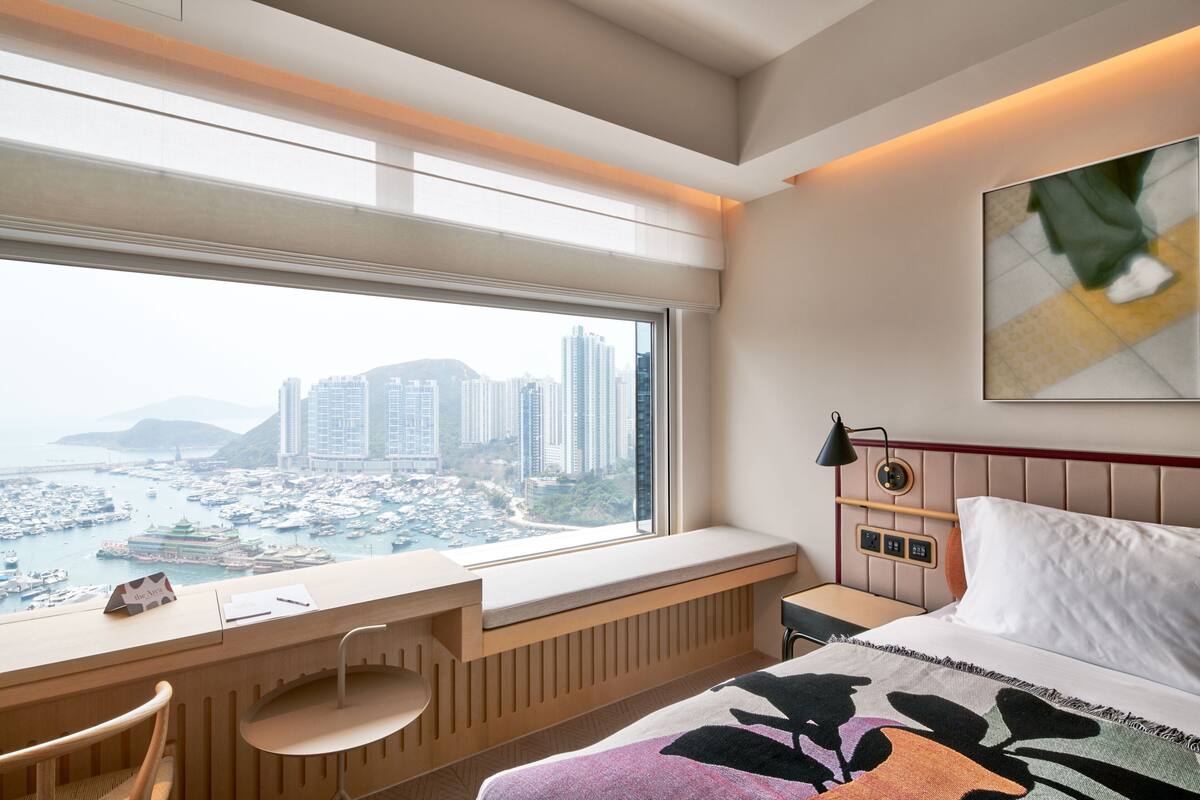 Una habitación de hotel con un ventanal grande, una cama, un escritorio y una silla.