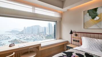 Une chambre d’hôtel avec une grande fenêtre, un lit, un bureau et une chaise.