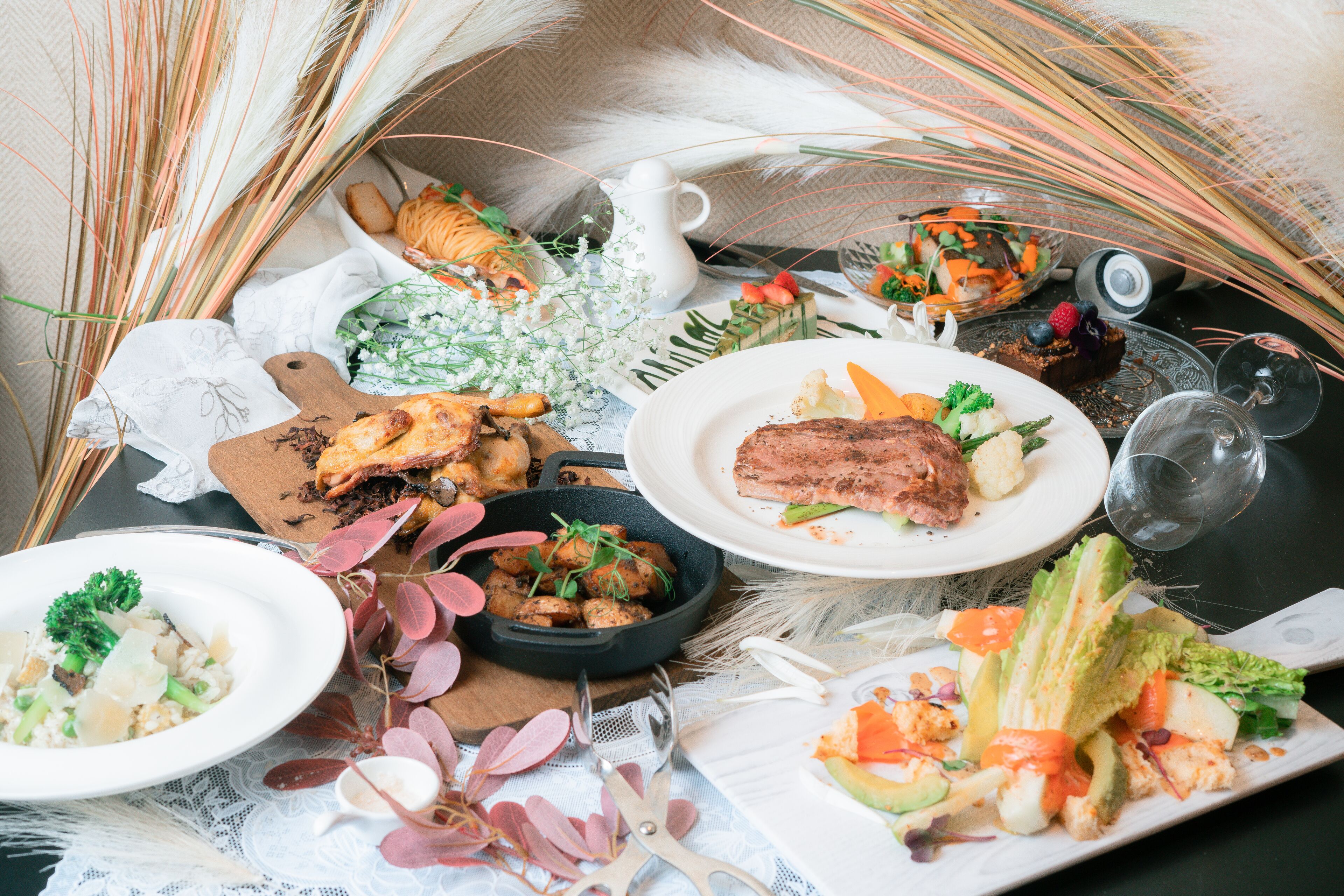 A table set with various dishes including a steak, salad, and bread, surrounded by decorative elements like feathers and flowers.