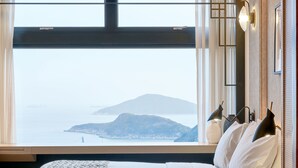 Un dormitorio moderno con una cama grande, vista al mar y una montaña al fondo.