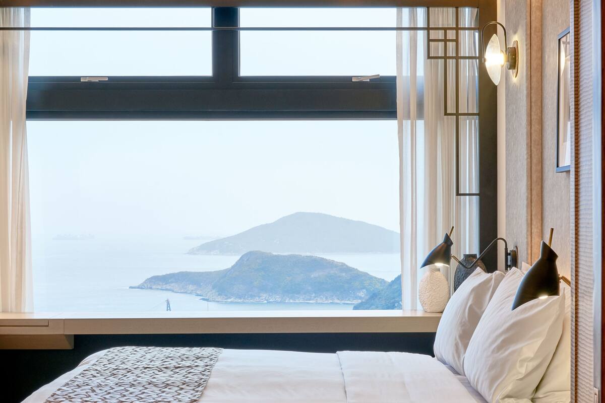 Un dormitorio moderno con una cama grande, vista al mar y una montaña al fondo.