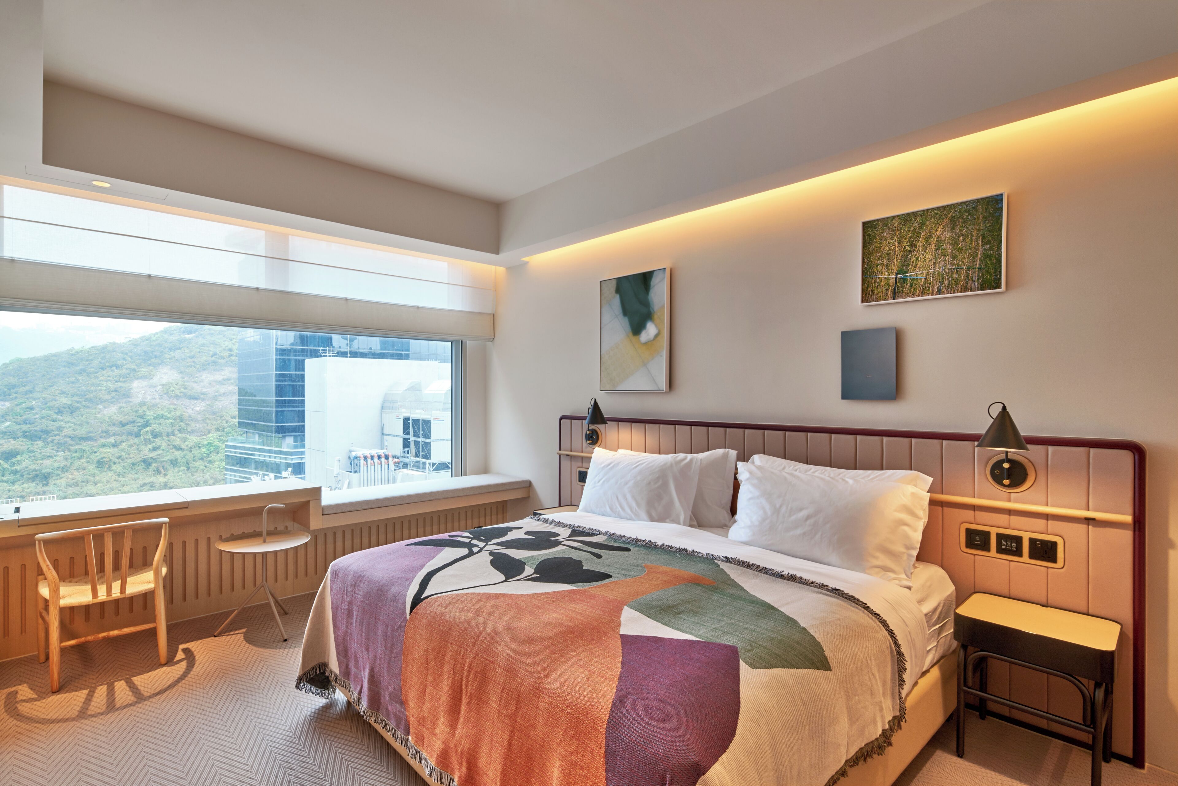 A hotel room with a large bed, a desk, and a chair. There is a window with a view of a mountain and a building.