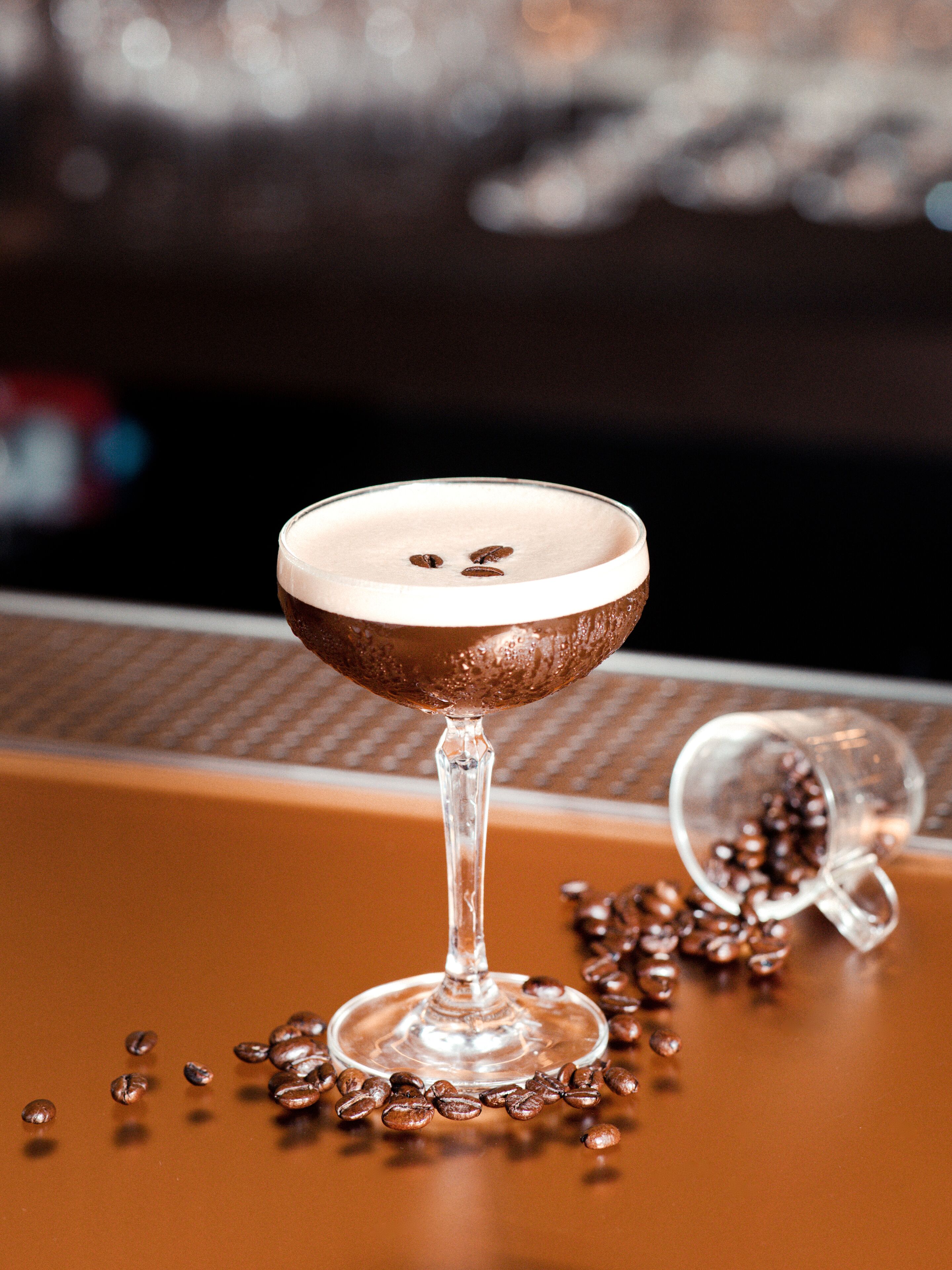 A glass with a frothy top, a coffee bean, and a spilled coffee container on a brown surface.