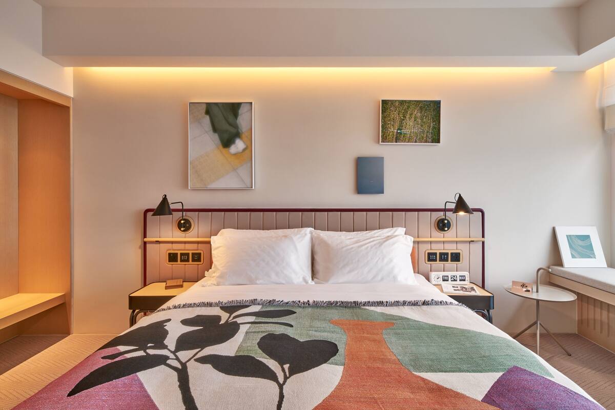 Una habitación de hotel moderna con una cama, mesitas de noche, un escritorio y obras de arte en las paredes.