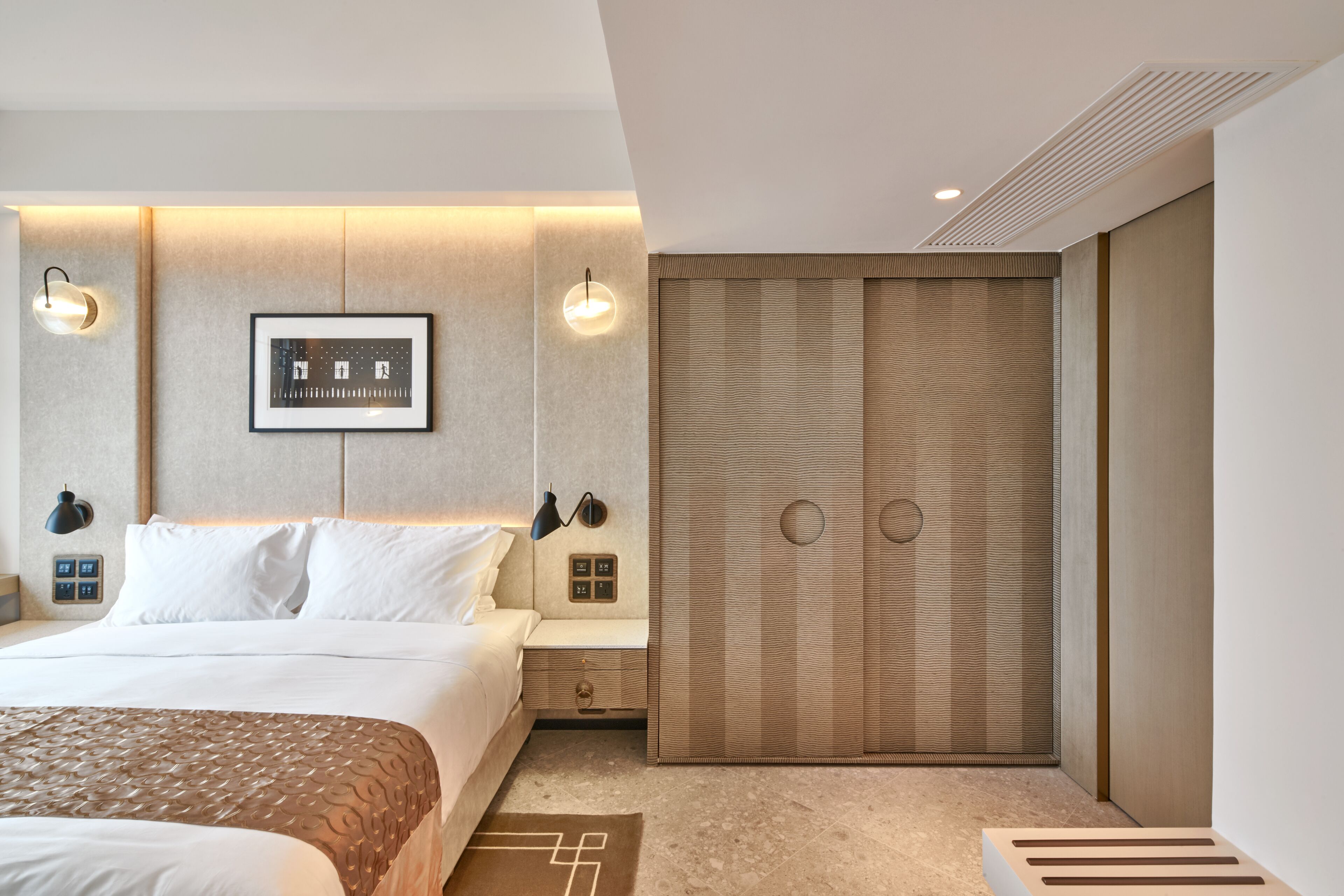 A modern hotel room with a large bed, a bedside table, a wardrobe, and a wall-mounted picture.