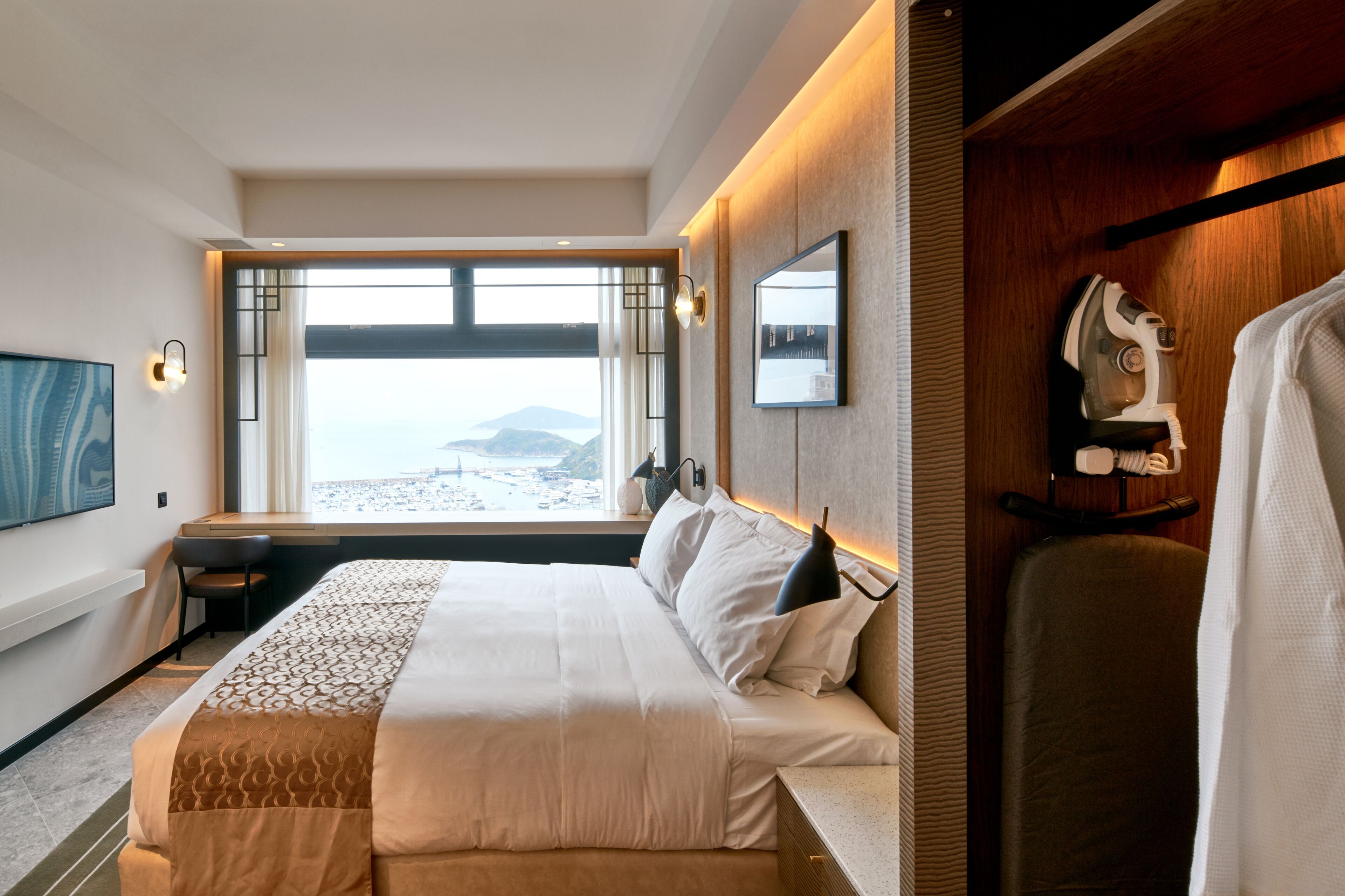 Quarto de hotel com uma cama grande, uma escrivaninha, uma cadeira, uma televisão e vista para a praia.