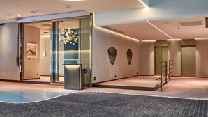 Un moderno vestíbulo de hotel con un mostrador de recepción, puertas de cristal y una escalera que conduce a los ascensores.