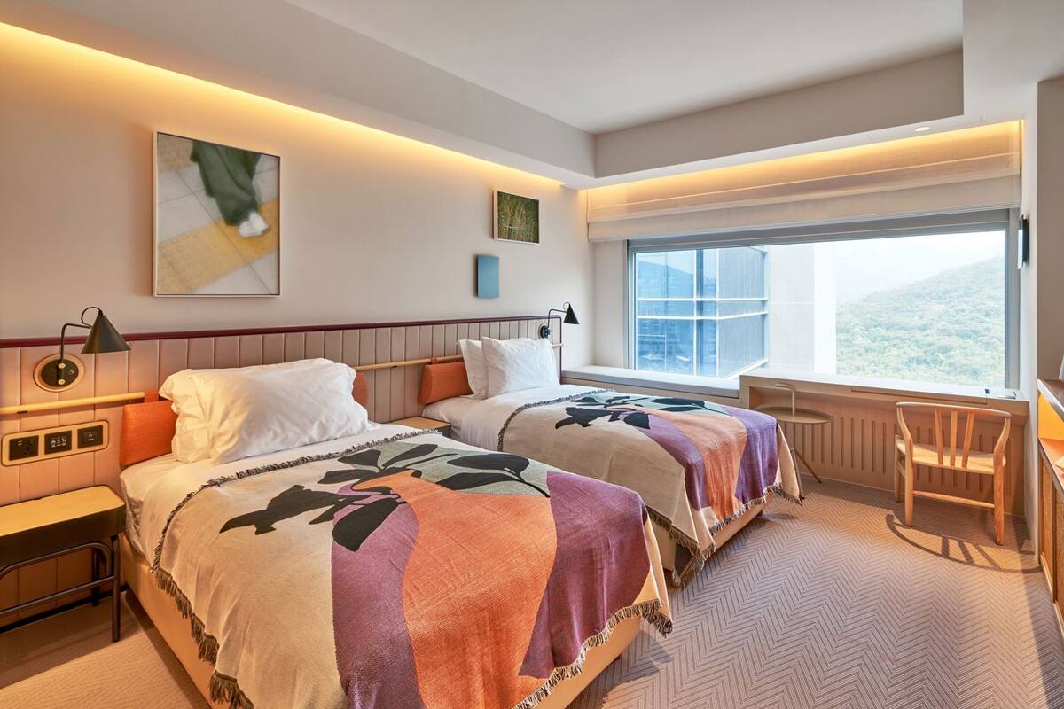 Habitación de hotel con dos camas, un escritorio, una silla, un ventanal con vistas y una obra de arte en la pared.