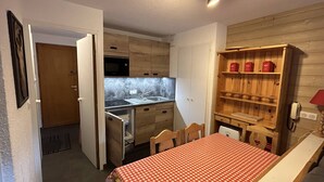 Kompakti keittiö, jossa on puukaapit, mikroaaltouuni ja pesuallas. Keittiössä on ruokapöytä, jonka päällä on ruutukuviollinen pöytäliina.