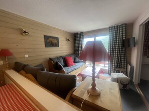 A cozy living room with a sofa, a wooden coffee table, a lamp, a television, and a window with curtains.