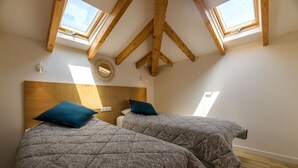 Ein Schlafzimmer mit zwei Betten, Holzbalken, Oberlichtern und einem Holz-Kopfteil.