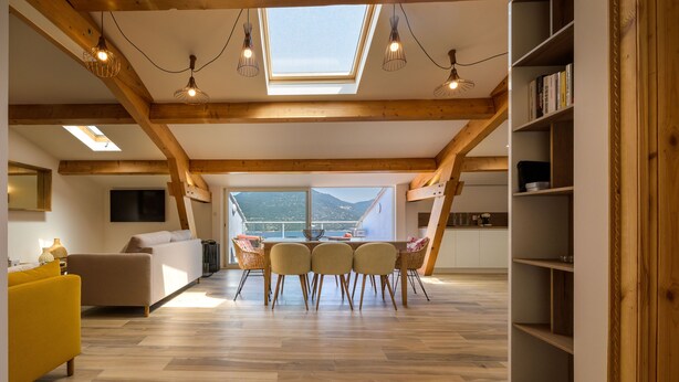 Ein großzügiges Loft mit Essbereich, Holzbalken, Dachfenster und Bergblick.