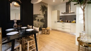 A dining area with a black table, white chairs, and a large mirror. There is a kitchen area with white cabinets and a stove. - CASA TAMARIT DUPLEX (Barcelona)