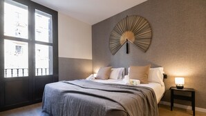 A bedroom with a bed, bedside table, wall art, and a window. - CASA TAMARIT DUPLEX (Barcelona)