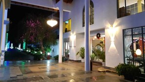 Entrada de hotel con patio adoquinado, columnas e iluminación decorativa.