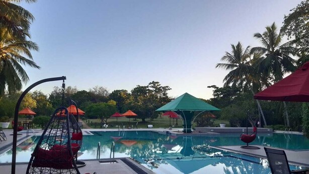 Zona de piscina con una hamaca colgante, sombrillas y sillones de descanso.