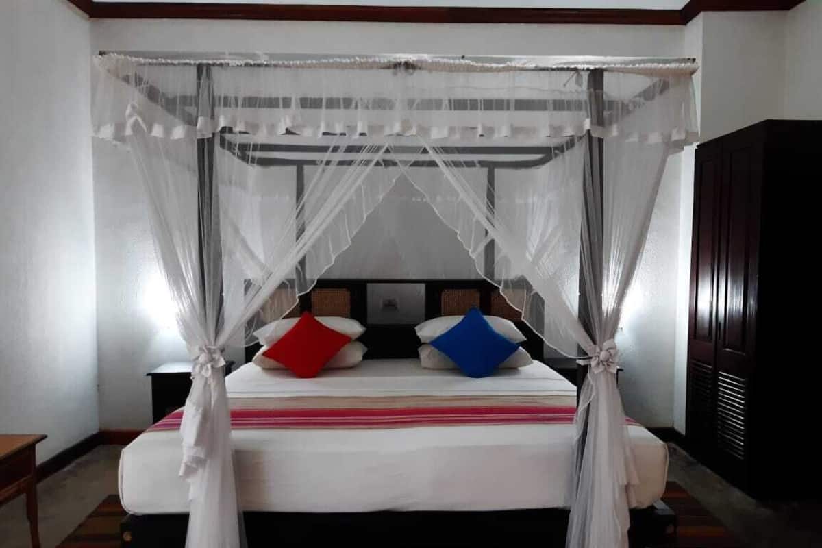 Una cama con dosel, almohadas, una mesita de noche y un armario.