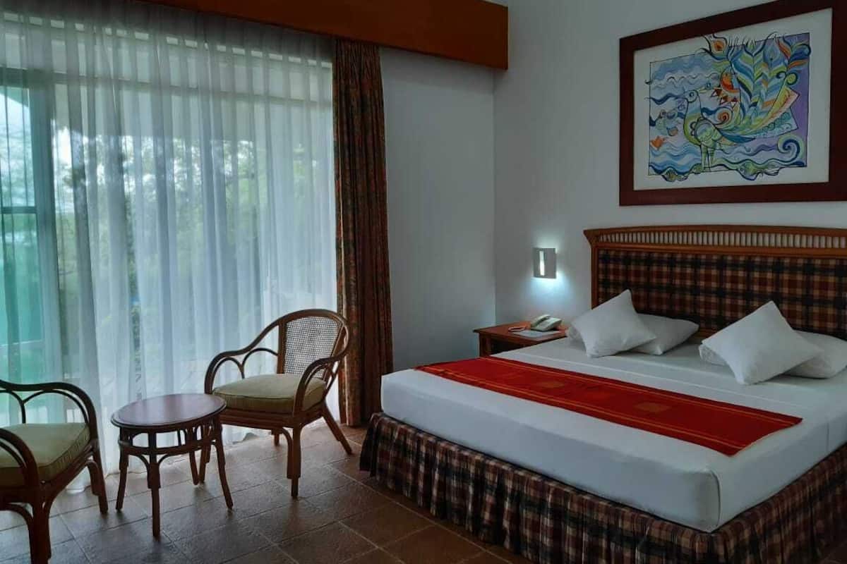Una habitación de hotel con una cama, una silla, una mesita, una mesita de noche y un cuadro en la pared.