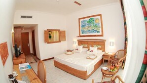 Habitación de hotel con una cama grande, cabecera de madera, una mesa de comedor y un pequeño rincón de estar con sillas.