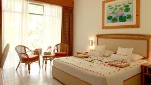 Habitación de hotel con una cama grande, dos sillas, una mesita y un cuadro de flores de loto en la pared.