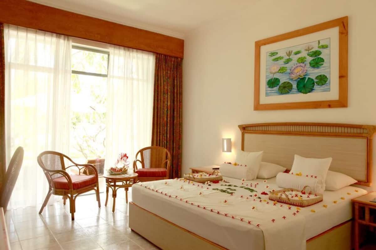 Habitación de hotel con una cama grande, dos sillas, una mesita y un cuadro de flores de loto en la pared.