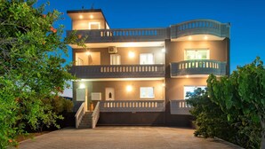 A multi-story building with a balcony on the second floor, a staircase leading to the entrance, and a well-lit facade. - Panoramic Sea Views, Pool, Garden, BBQ, TableTennis, Playground, Hammock (Chania)