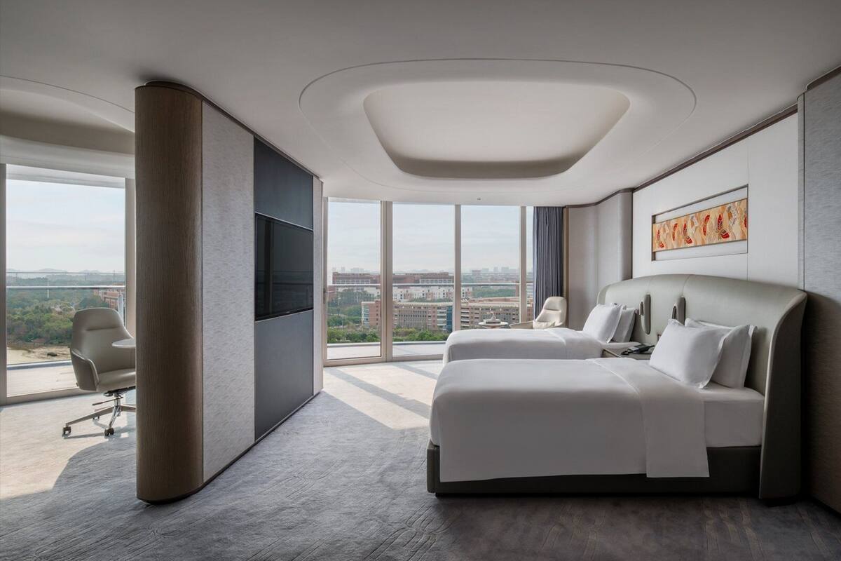 A modern hotel room with a large bed, a TV, and a city view.