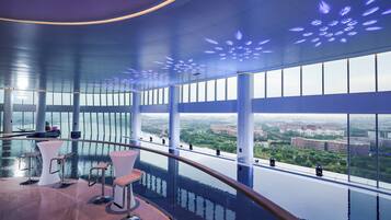 A modern interior with a curved balcony, large windows, and a view of the cityscape.