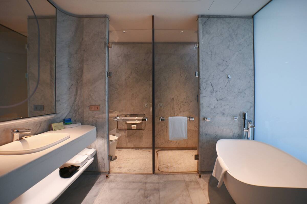 A modern bathroom with a large mirror, a bathtub, a shower enclosure, and a toilet.