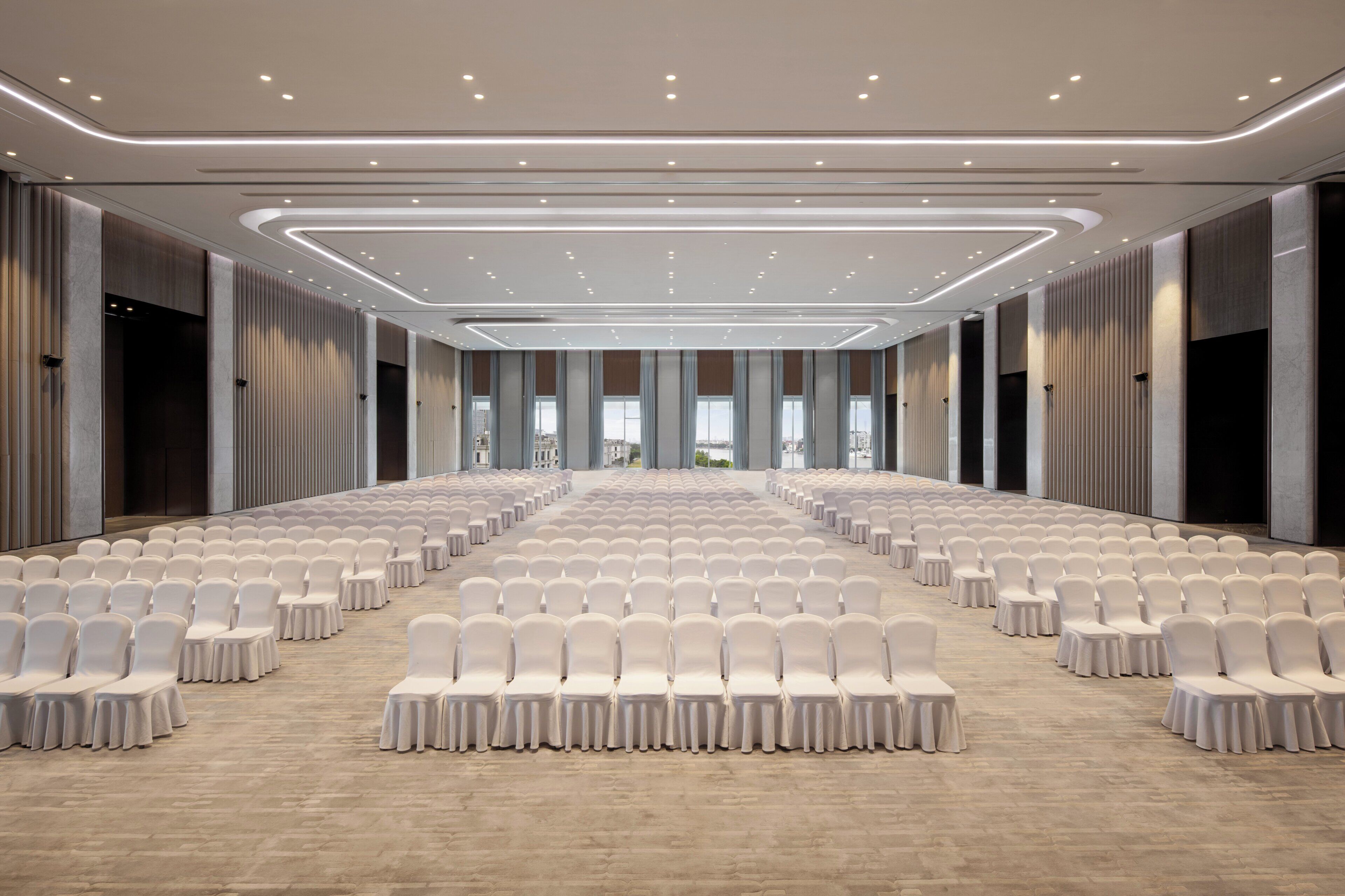 Une grande salle de conférence avec des rangées de chaises blanches et un plafond au design moderne.