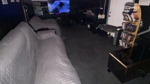 A dimly lit room with a large screen, a couch, and a bookshelf. - Artist Housing - Hostel (Los Angeles)