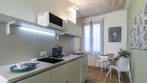 Uma cozinha compacta com micro-ondas, chaleira e pia. Possui um espaço de refeições com mesa e cadeiras.