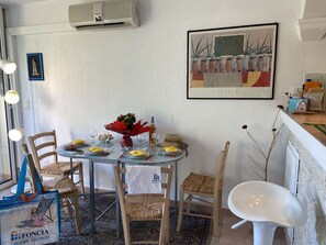 A dining area with a round table set for two, surrounded by wooden chairs. A decorative vase with red flowers is on the table.