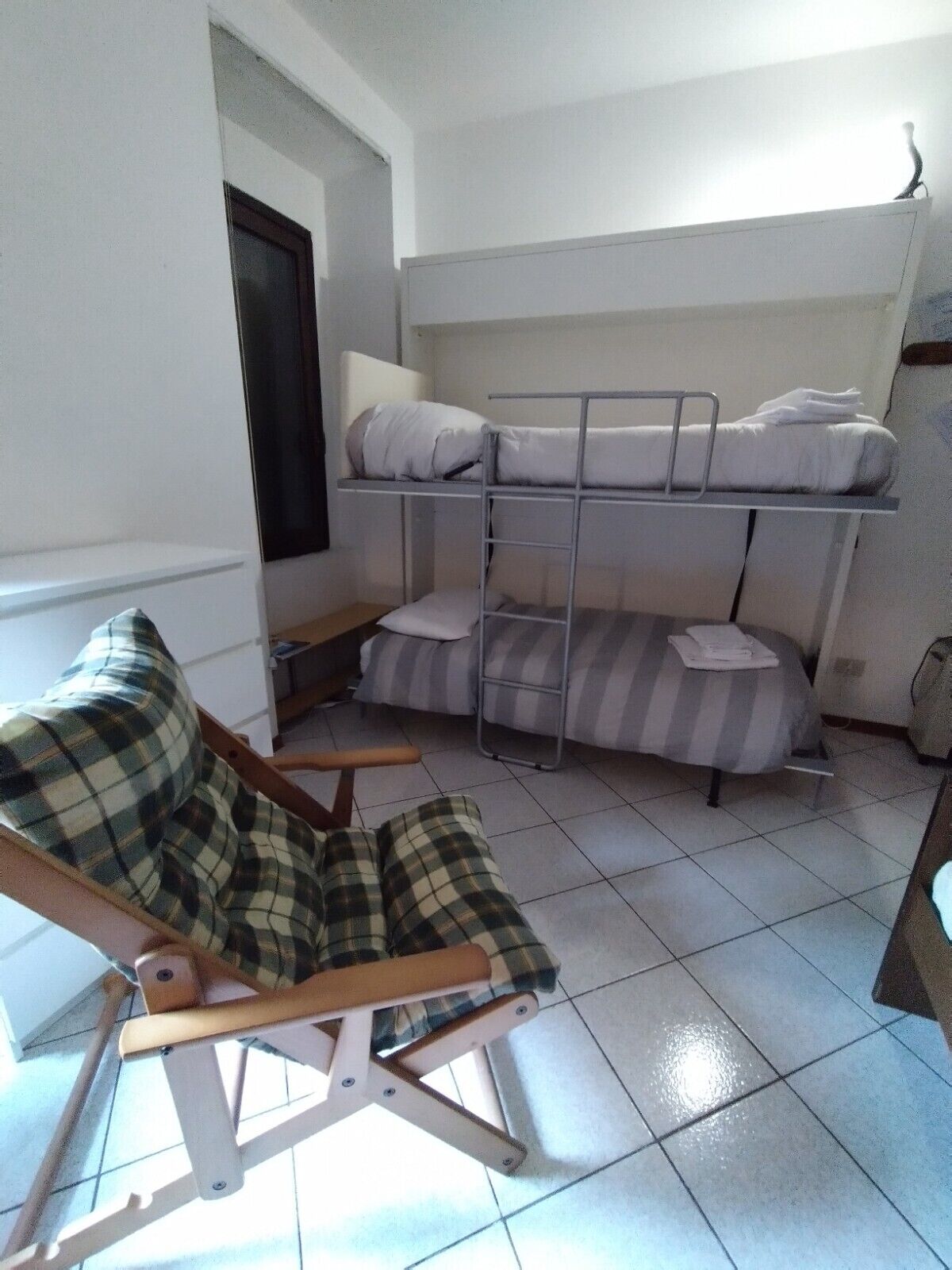 Une chambre avec un lit superposé, un lit simple et une chaise.