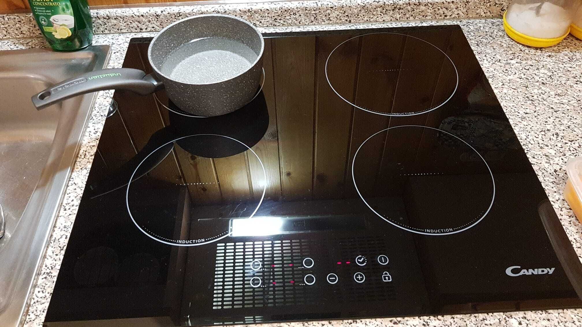 A black induction cooktop with three circular induction zones and a pot on one of the zones.