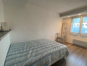 A bedroom with a bed, a chair, a radiator, and a window with heart-shaped decorations.