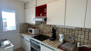 Una cocina compacta con microondas, horno, cafetera y un ventanal pequeño.