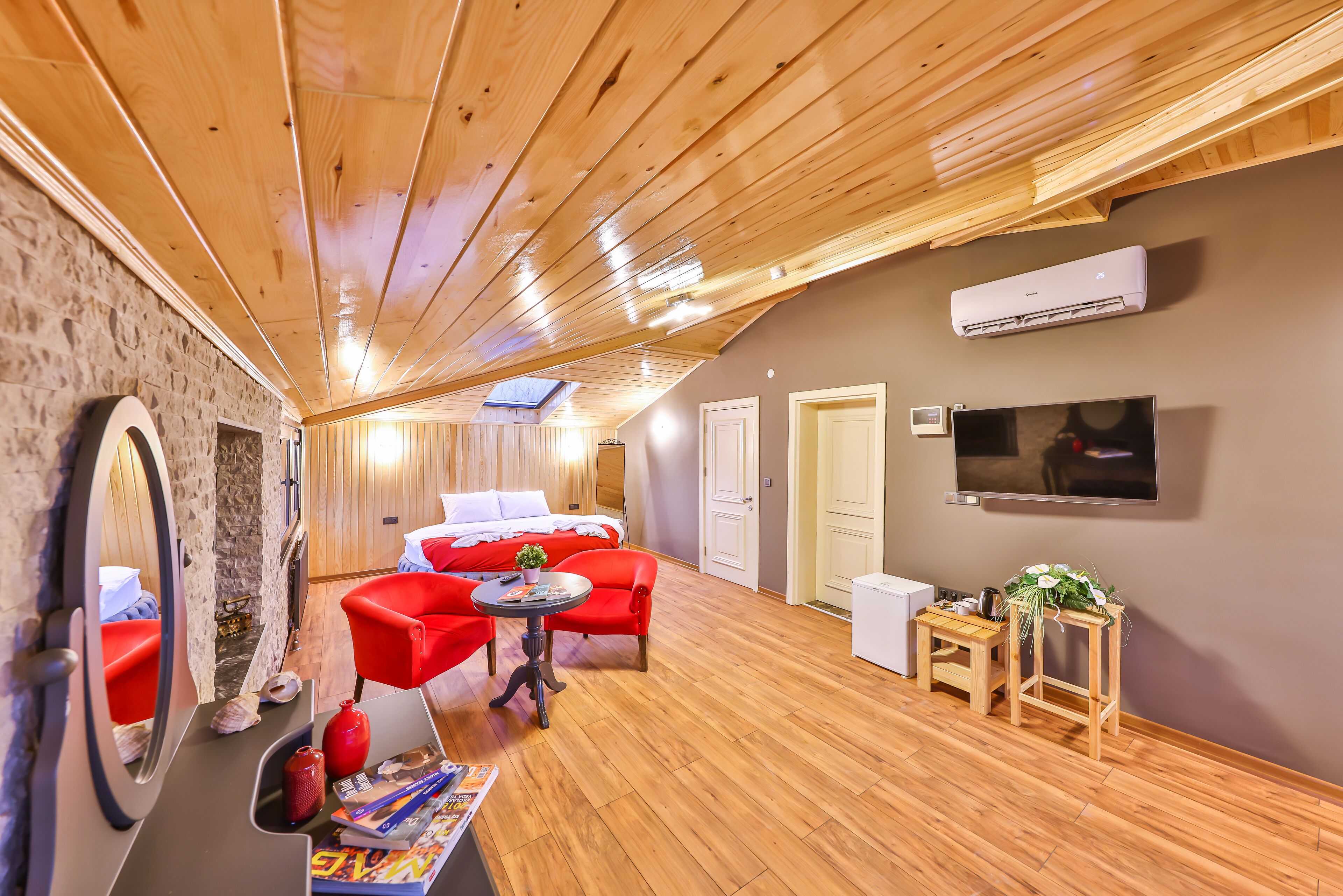 Una habitación acogedora con techo de madera, una cama, un sofá rojo, una mesita y un televisor.