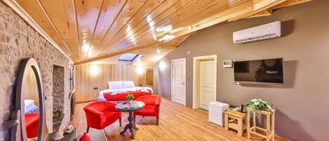 Una habitación acogedora con techo de madera, una cama, un sofá rojo, una mesita y un televisor.