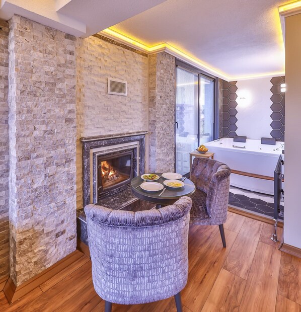 A cozy room with a stone fireplace, a dining table with chairs, and a view of the city through large windows.